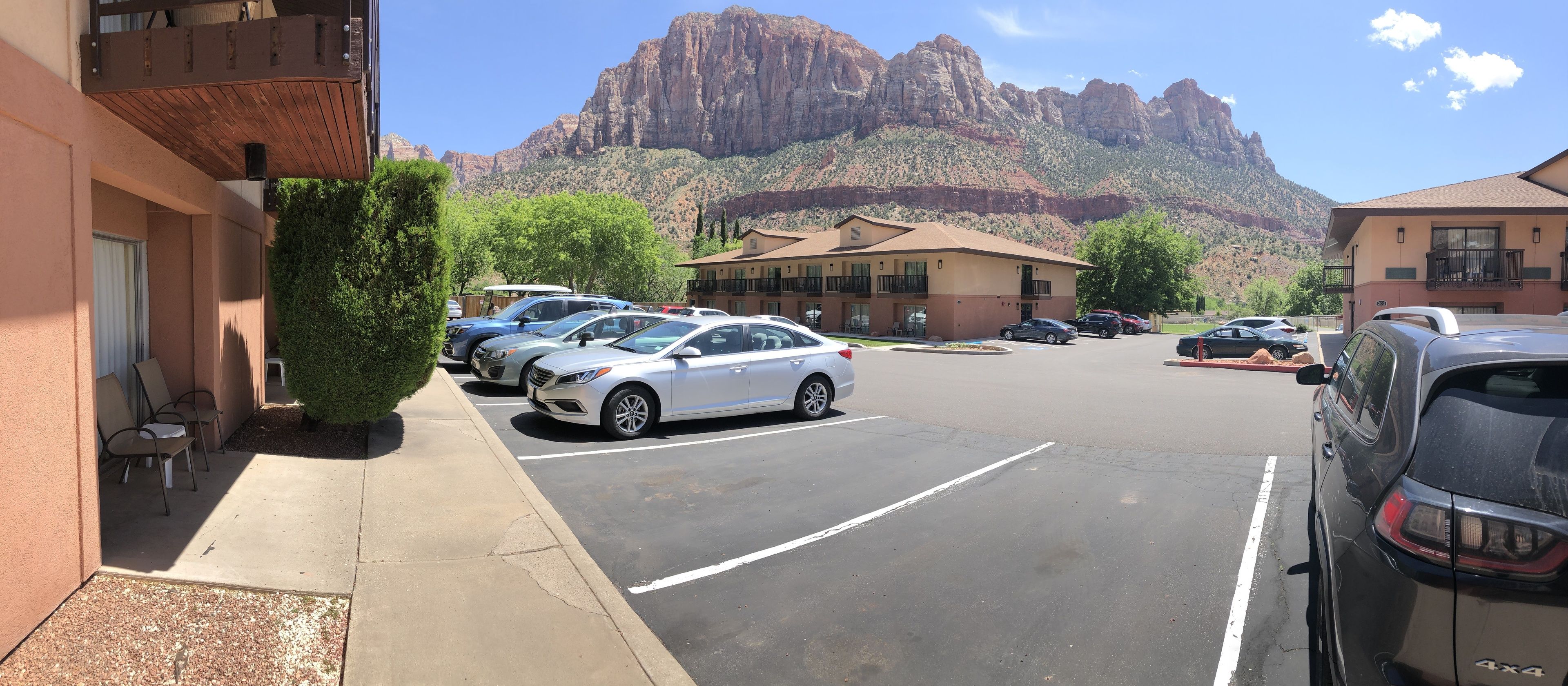 Un estacionamiento con varios coches, un edificio de techo plano y una montaña al fondo.