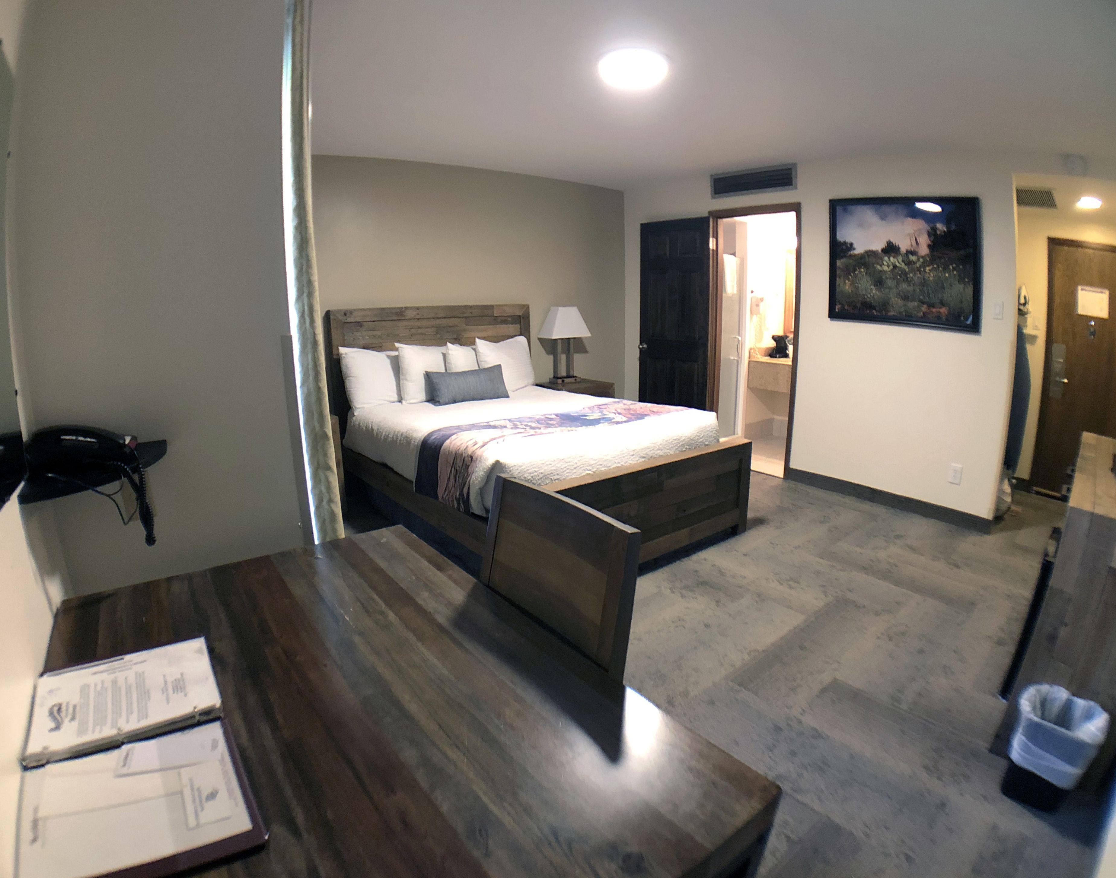 Une chambre d’hôtel avec un lit en bois, un bureau avec une chaise, un téléphone et un tableau accroché au mur.
