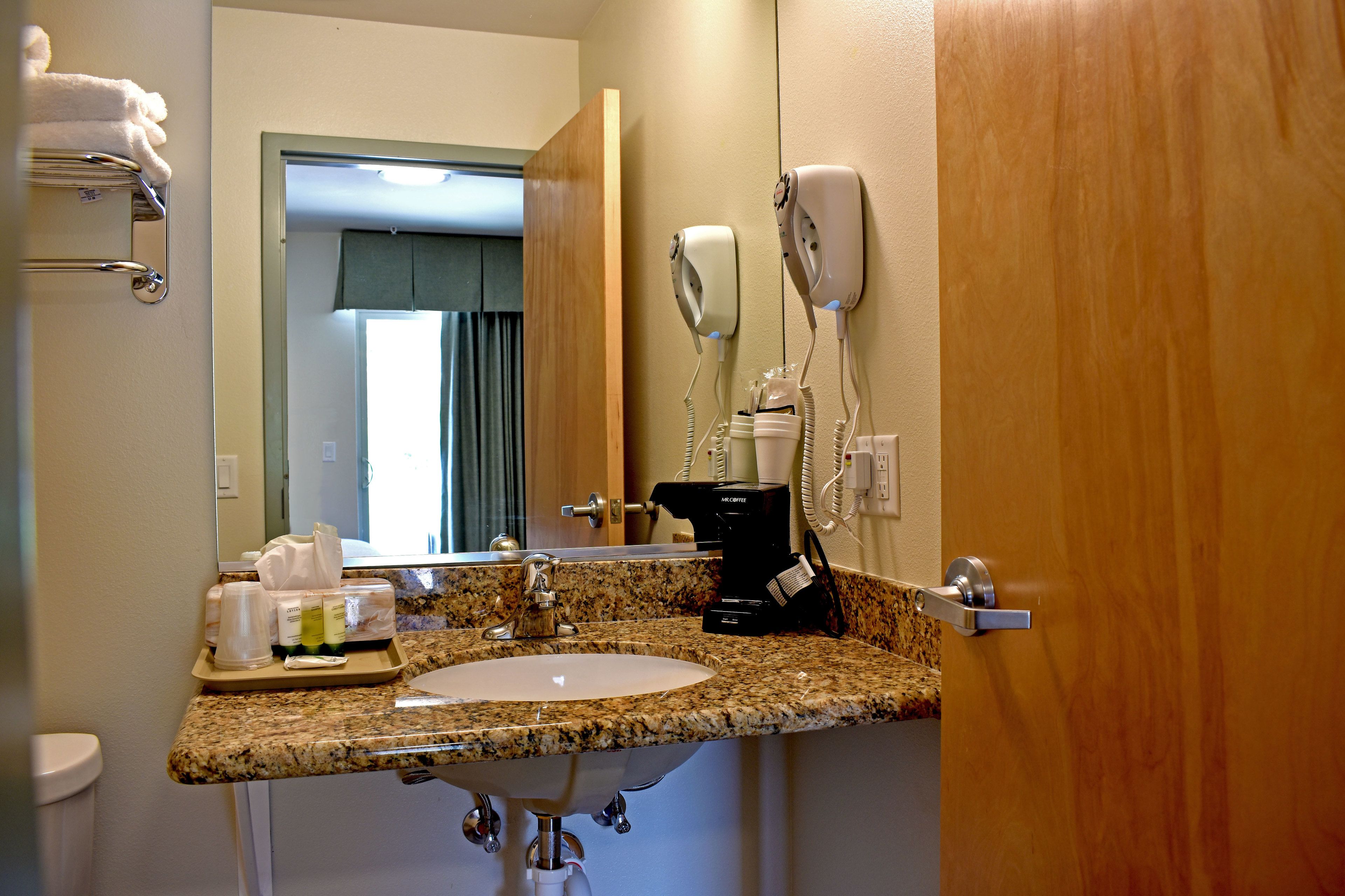 A bathroom with a granite countertop sink, a hairdryer, a coffee maker, and a towel rack.