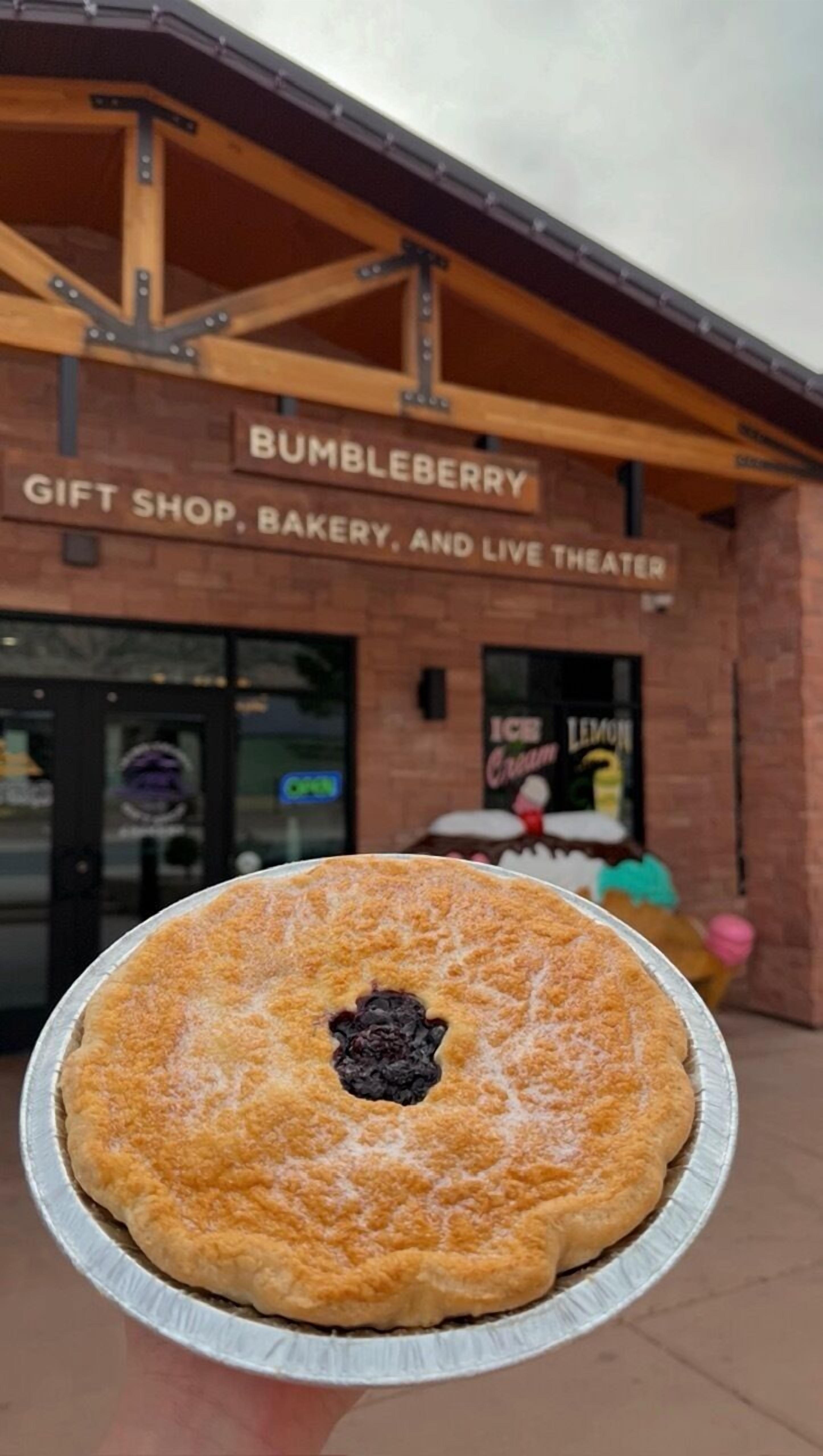 Une tarte dans un récipient en aluminium, devant un bâtiment sur lequel est apposée une enseigne indiquant : « BOUTIQUE DE CADEAUX BUMBLEBERRY, PÂTISSERIE ET SALLE DE SPECTACLE ».