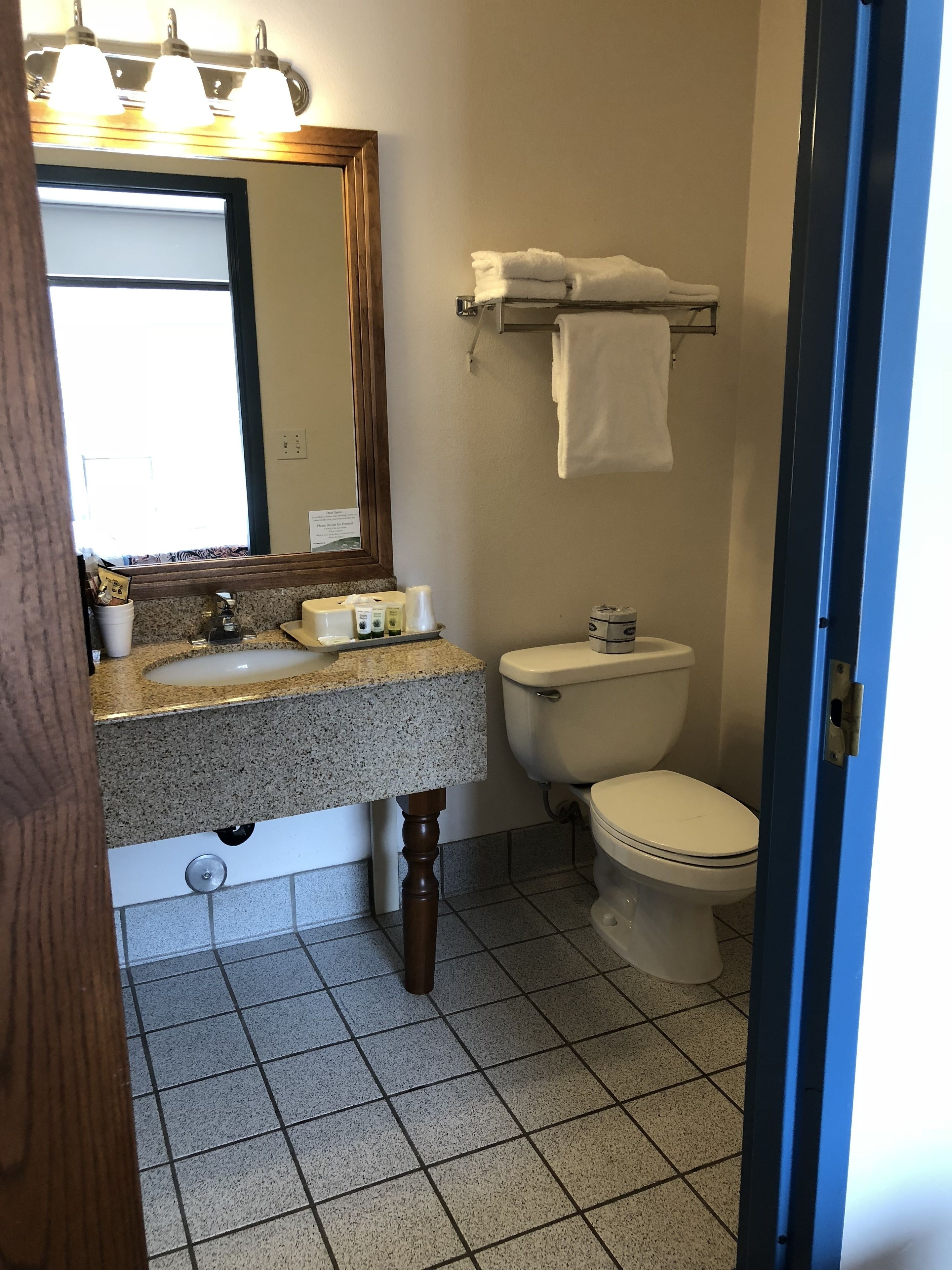 Un baño con encimera de granito, inodoro, toallero y espejo.
