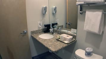 Une salle de bain d’hôtel avec un lavabo doté d’un plan de travail en granit, un miroir, des toilettes et un porte-serviettes.