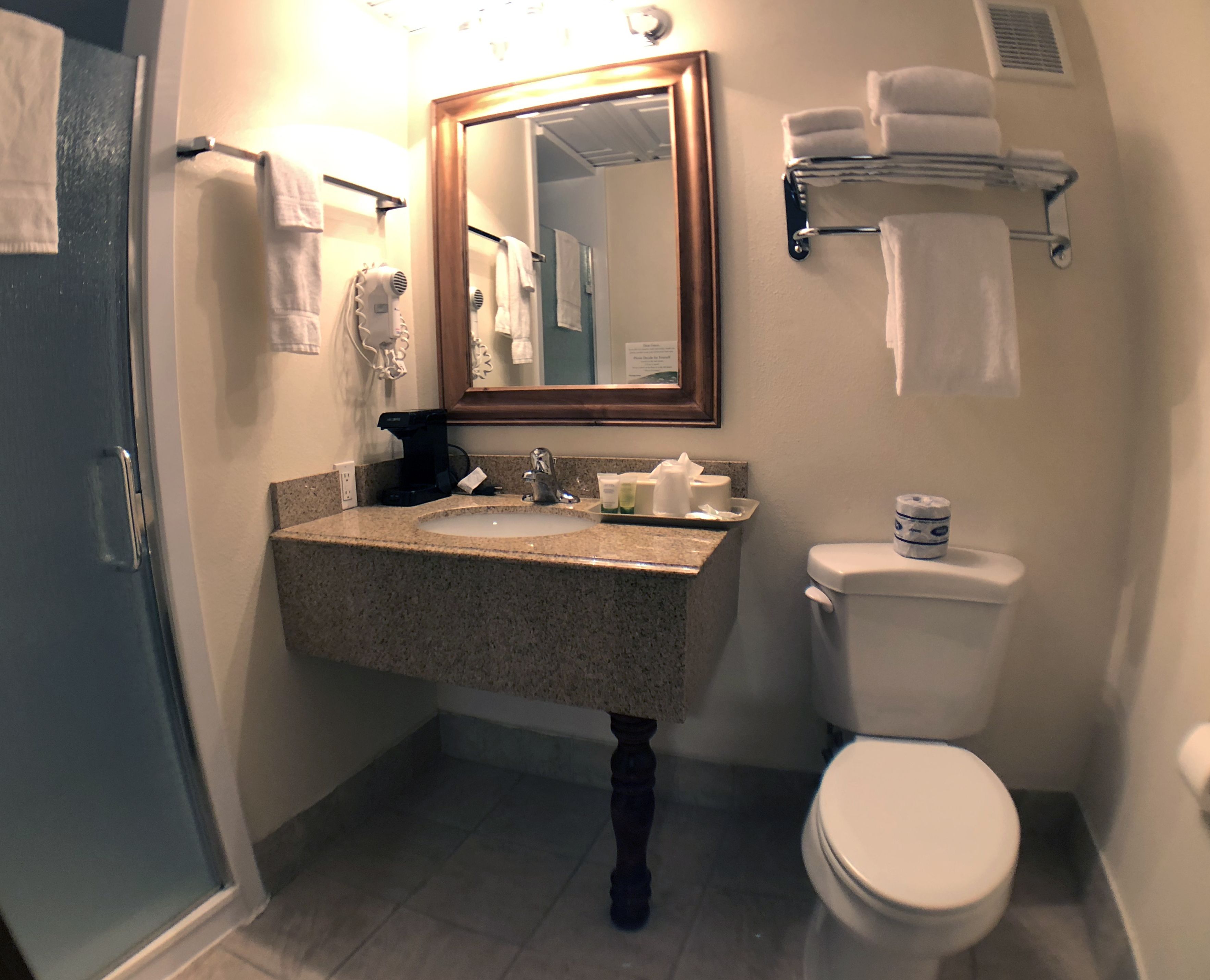 A bathroom with a sink, mirror, and toilet. There are towels on the wall and a towel rack.