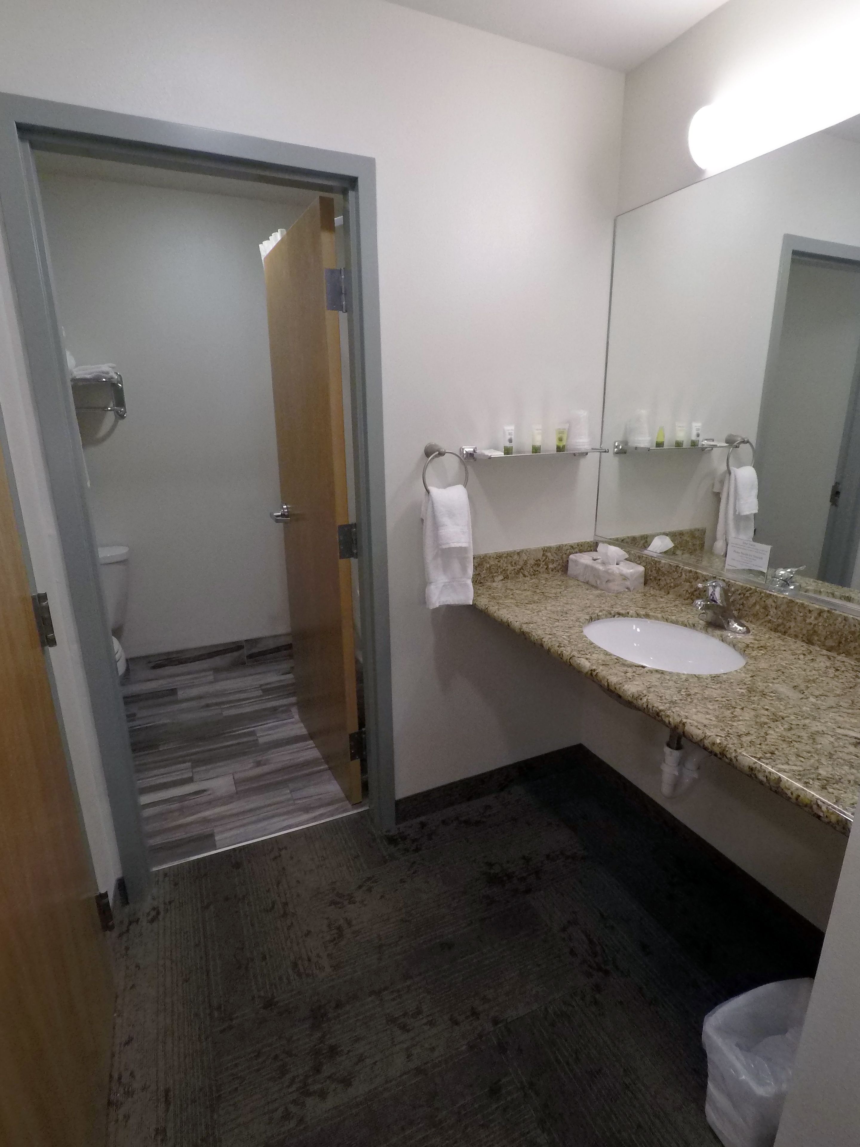 Casa de banho de hotel com lavatório, espelho, porta-toalhas e artigos de higiene pessoal.