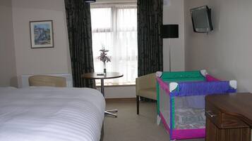 Habitación de hotel con cama, una mesita con un jarrón, una silla, televisión y una litera.