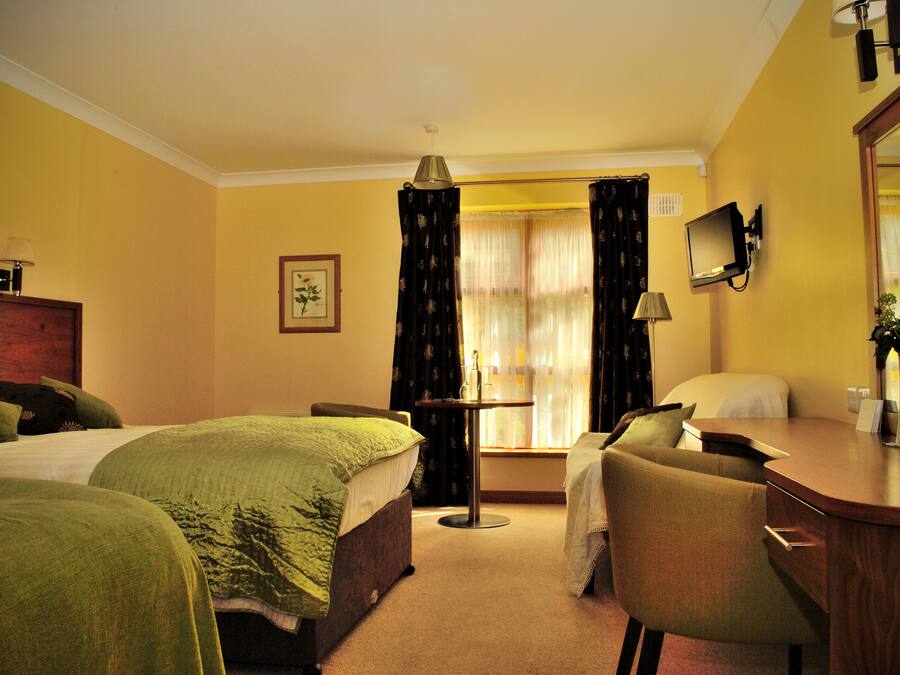 A hotel room with two beds, a desk, a chair, a TV, and a window with curtains.