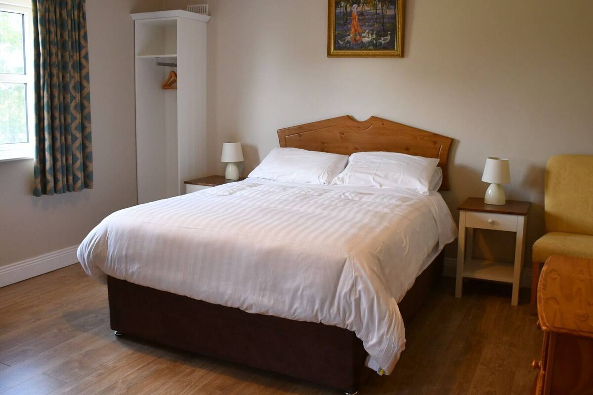 A neatly made bed with white linens, a wooden headboard, and two bedside tables with lamps.