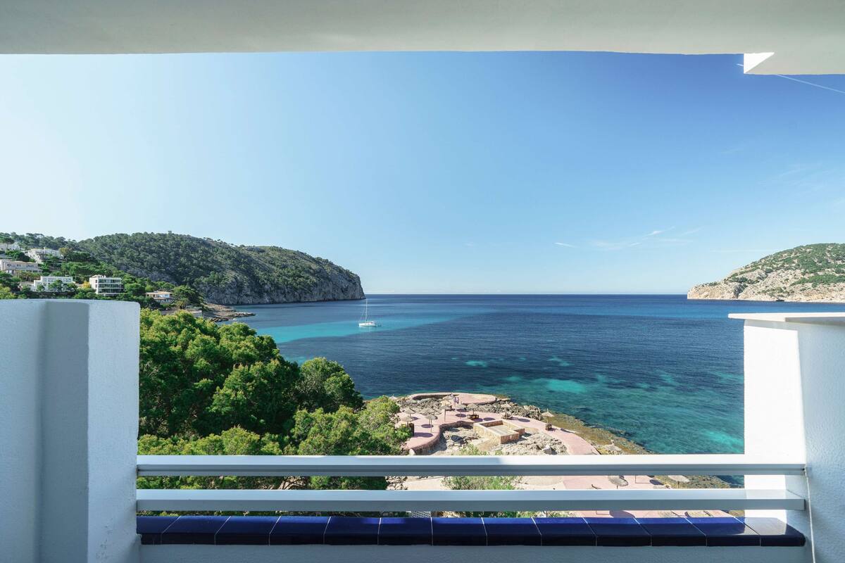 A balcony with a view of a coastal area, including a rocky beach and a clear blue sea.