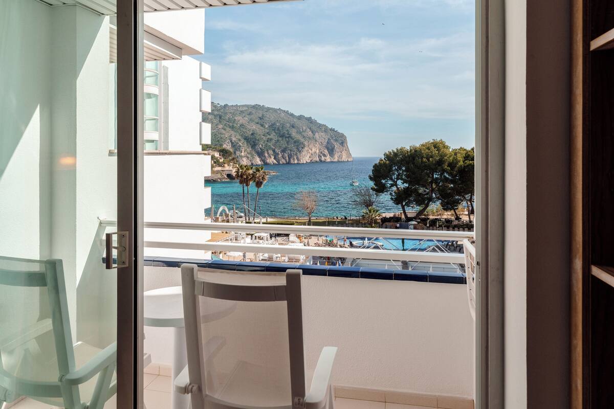 A balcony with a view of the sea, a chair, and a pool area.