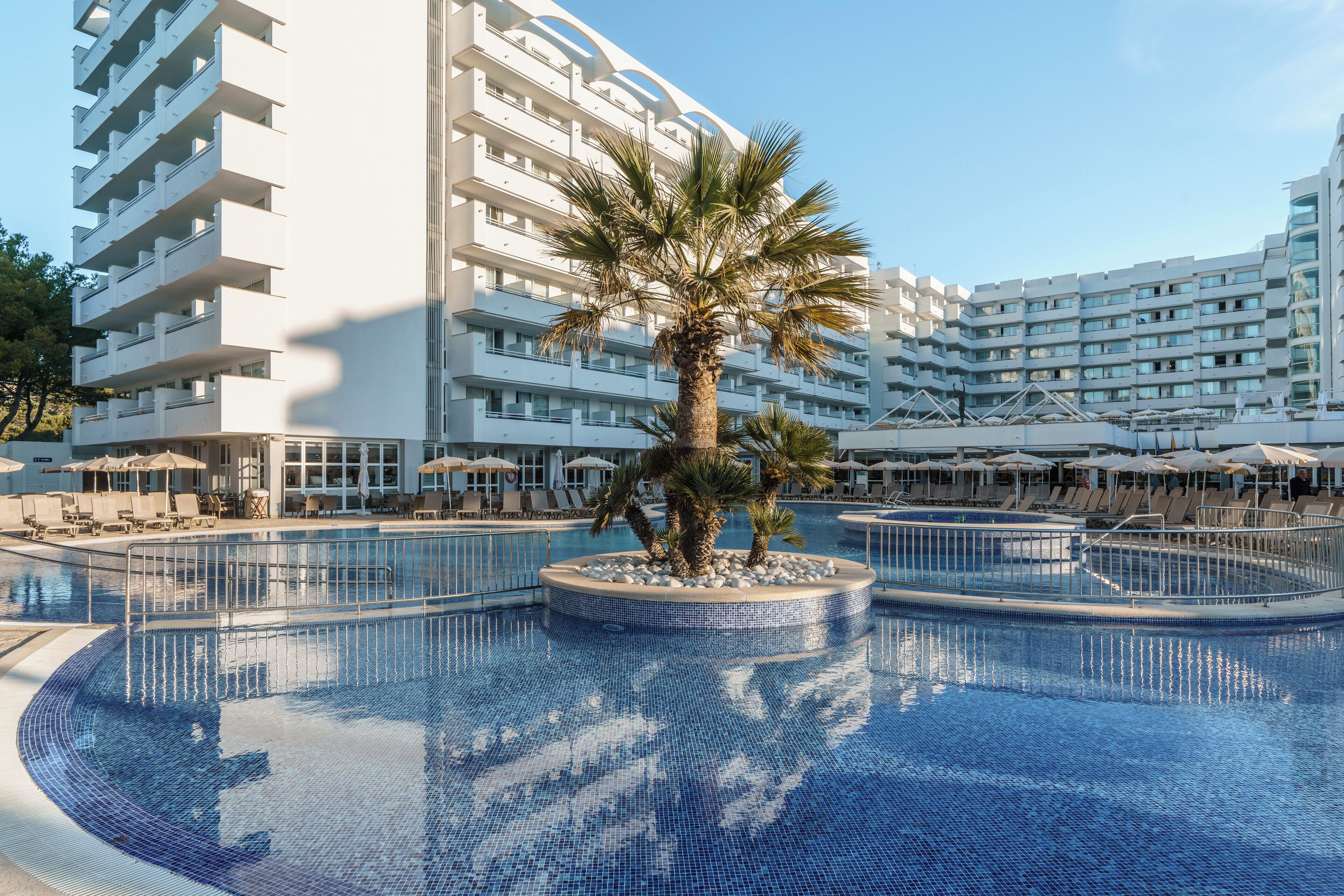 Un hotel moderno con piscina central, varios balcones y zonas de estar al aire libre.