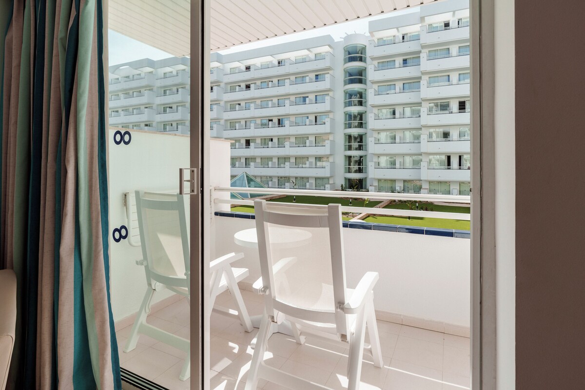 A balcony with white chairs and a table, overlooking a modern apartment building.