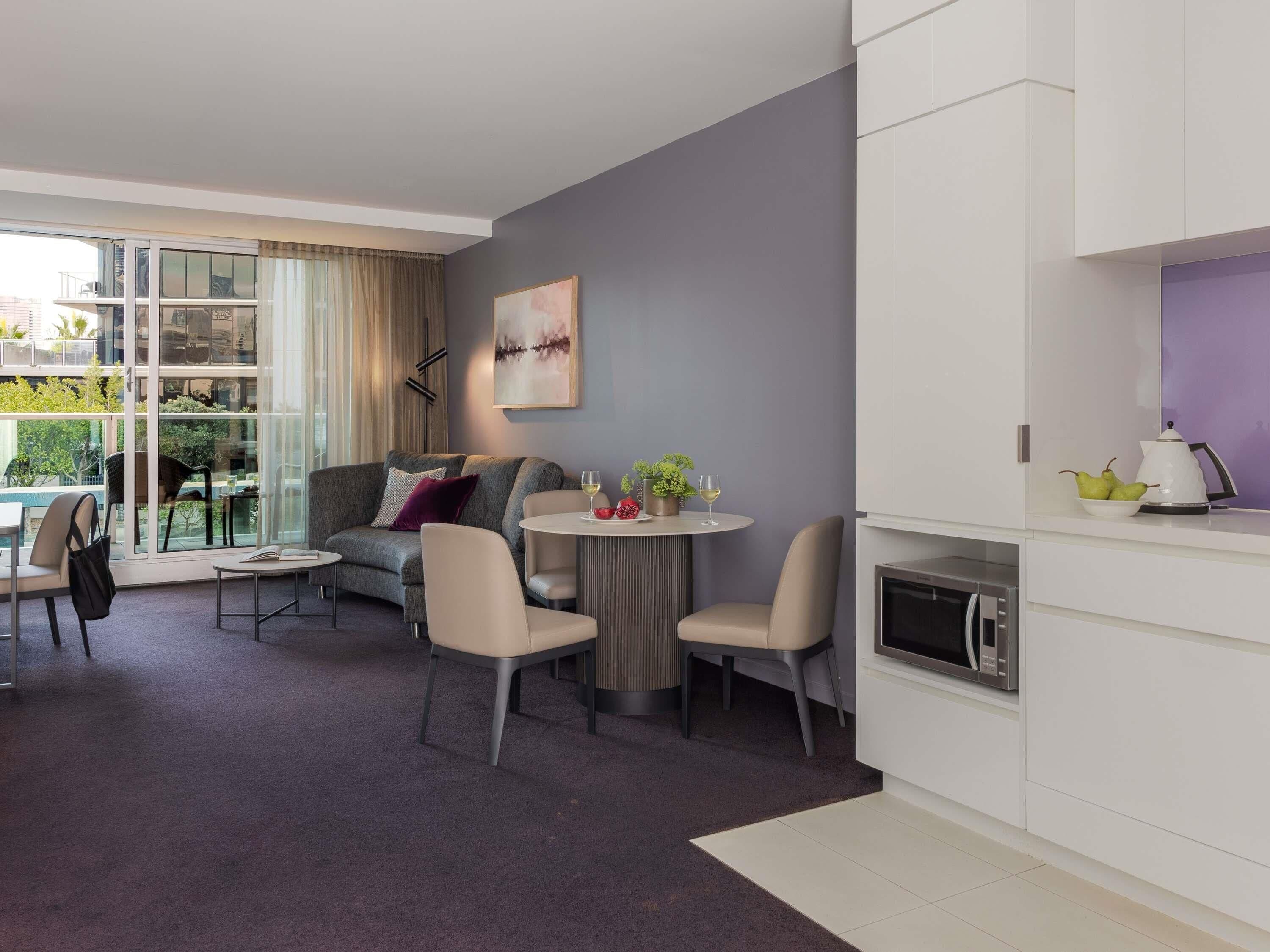 A modern living room with a sofa, chairs, a dining table, and a kitchen area with a microwave.