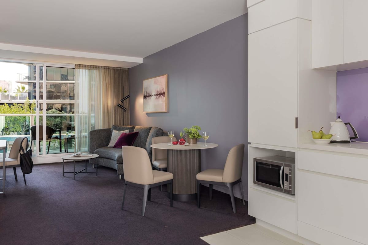 Een moderne woonkamer met een bank, stoelen, een eettafel en een keukenhoek met een magnetron.