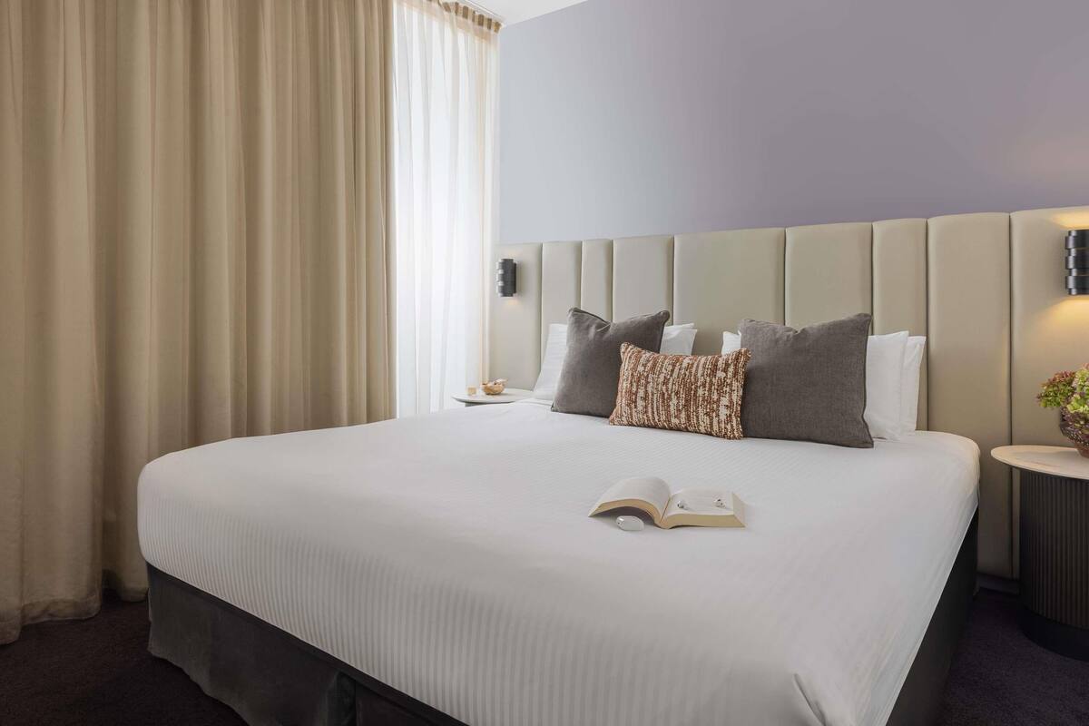 Een hotelkamer met een groot bed, een nachtkastje, een wandlamp en een raam met gordijnen.