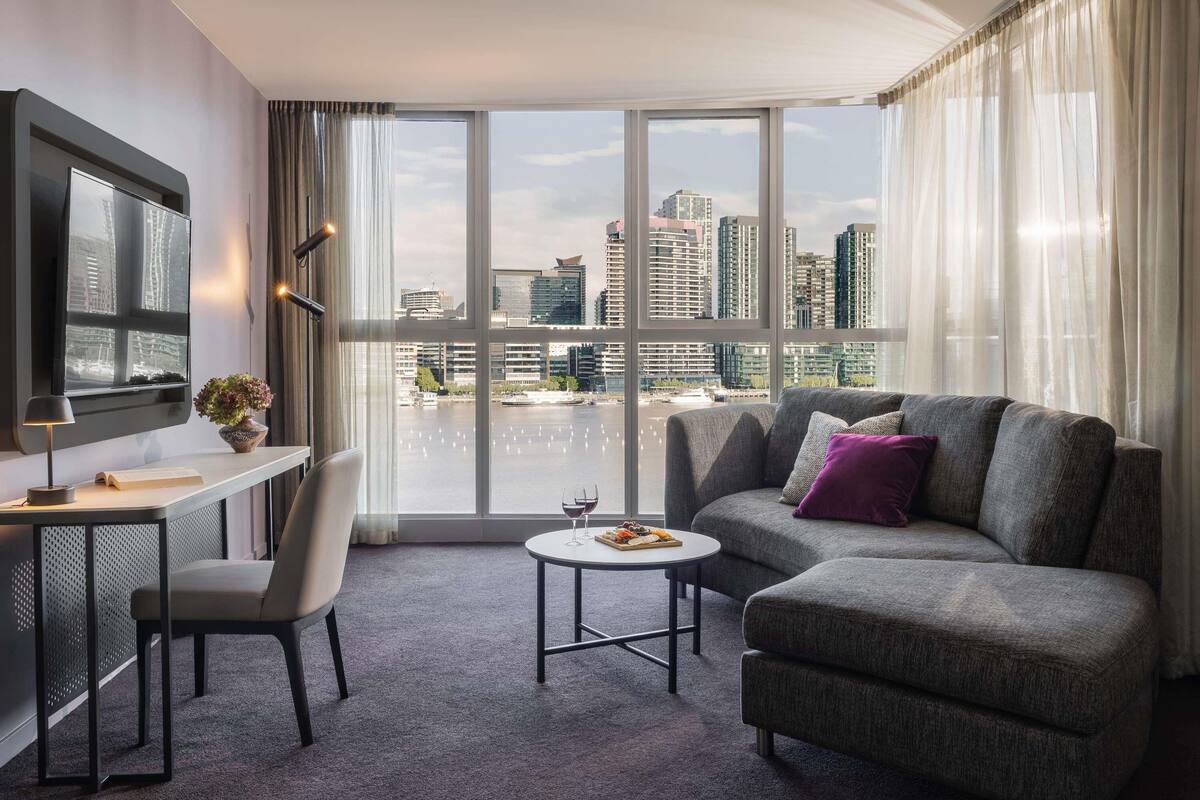Een moderne hotelkamer met een groot raam, een flatscreen televisie, een bureau met stoel, een bank en een kleine salontafel.