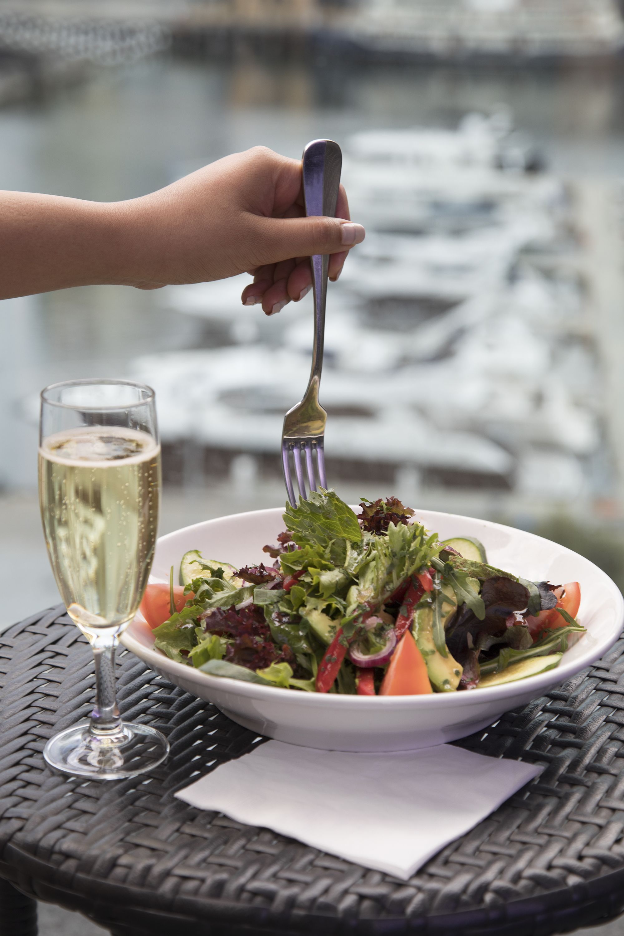 A bowl of salad with a fork on a table with a glass of champagne.
