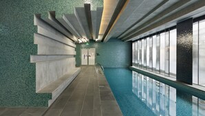 Una piscina interior moderna amb sòl de rajola, barana de vidre i sostre amb llums lineals.