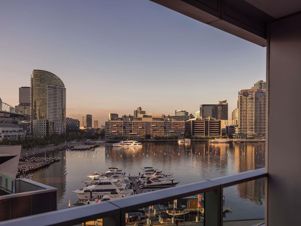 A marina with boats docked, a city skyline in the background, and modern buildings.