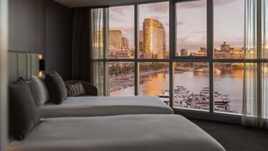 Habitació d'hotel amb un finestral gran que ofereix vistes a l'horitzó urbà i un riu.