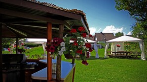 A covered outdoor area with a grill, a table, and hanging flowers. - Hotel Waldblick (Donaueschingen)