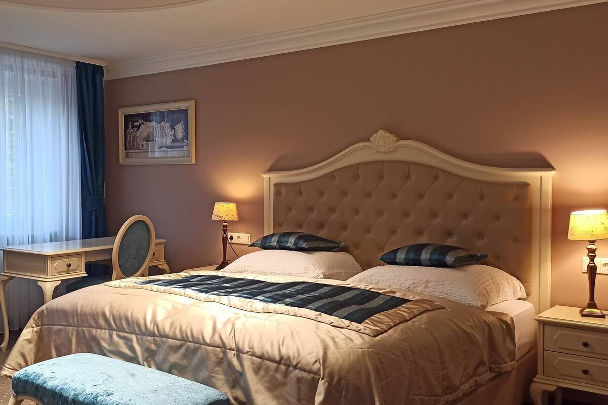 A hotel room with a large bed, a desk, a chair, and a small table.