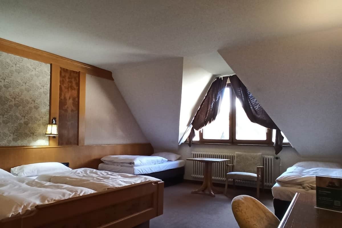 A hotel room with two beds, a small table, a chair, and a radiator.