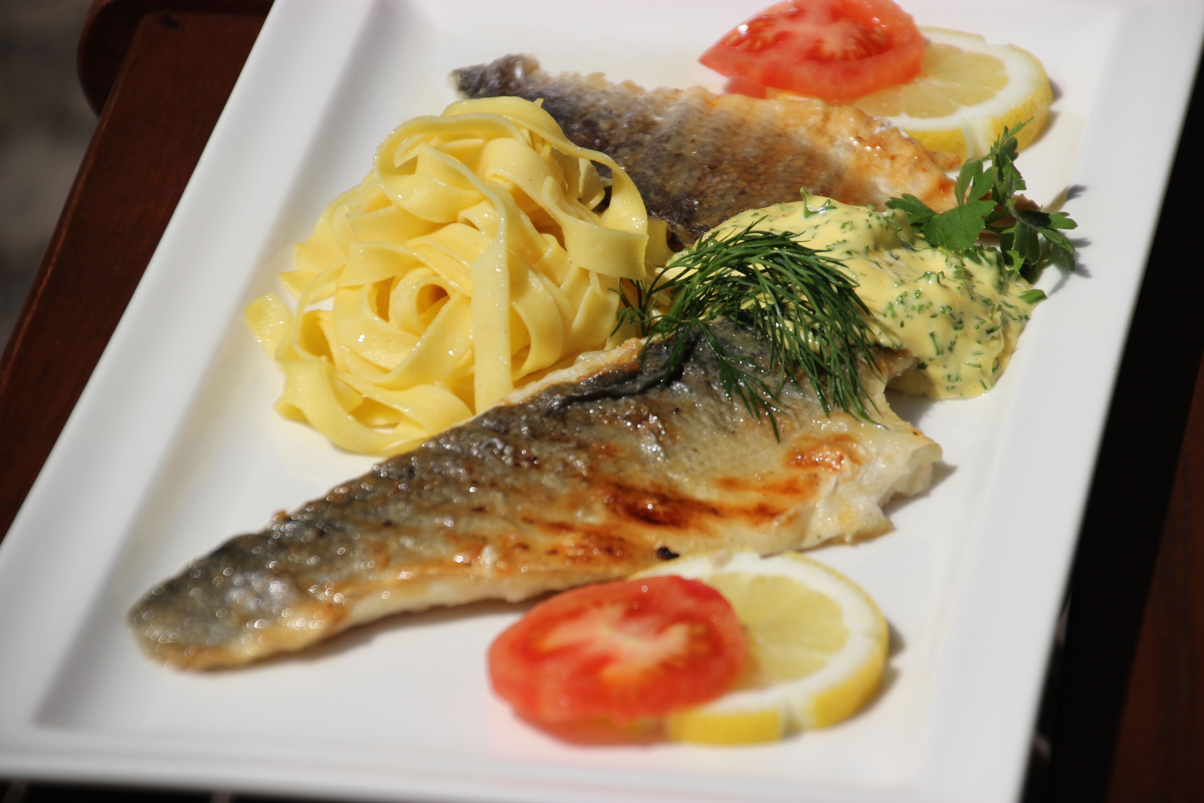 Un plato con pescado a la parrilla, rodajas de limón y una porción de pasta adornada con hierbas.