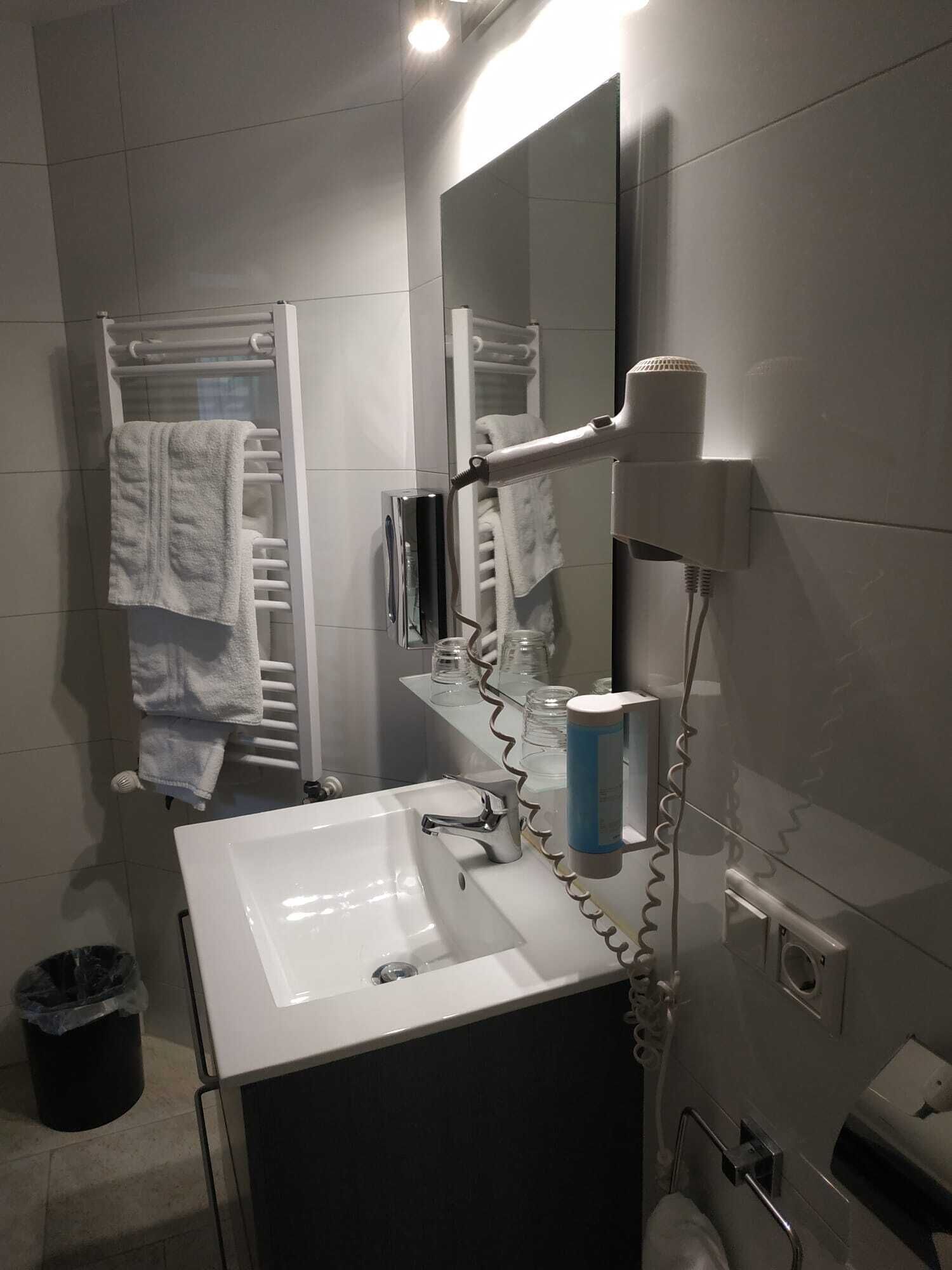 Un baño moderno con un lavamanos blanco, un secador de pelo y un perchero para toallas.