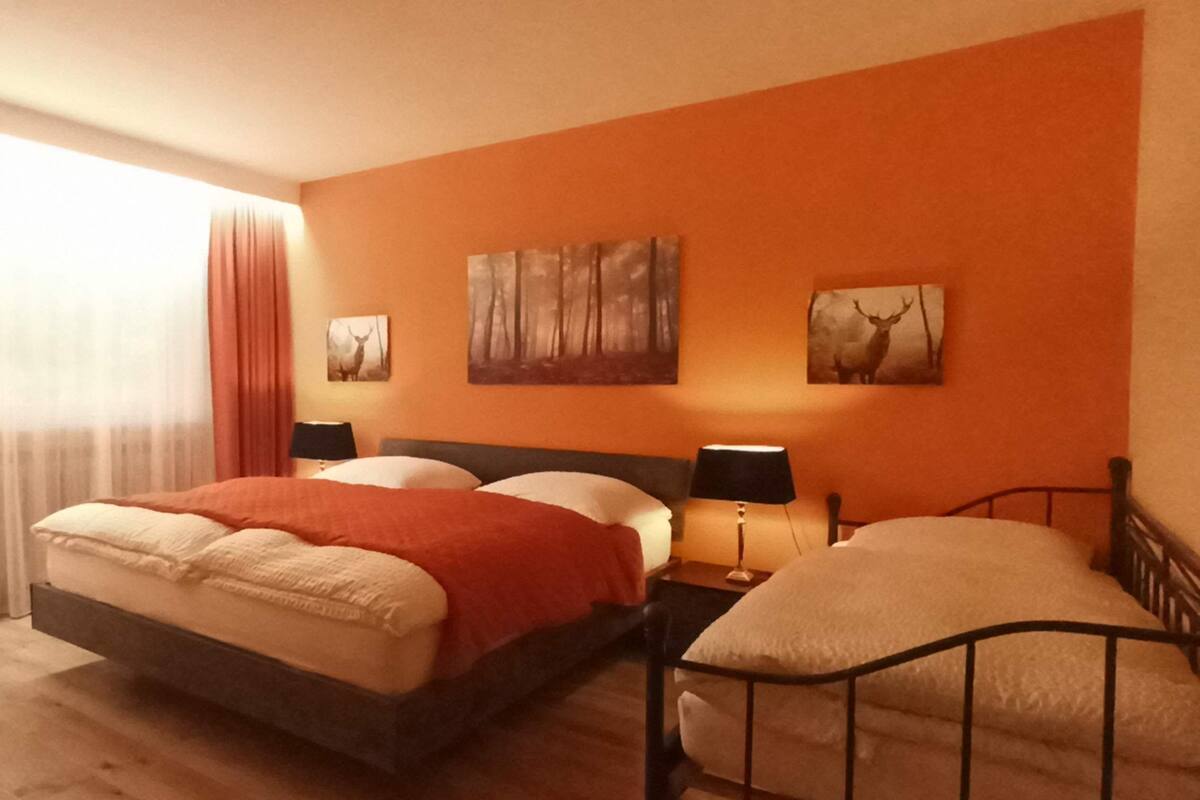 A bedroom with a bed, two bedside tables, a window with curtains, and two wall-mounted paintings.