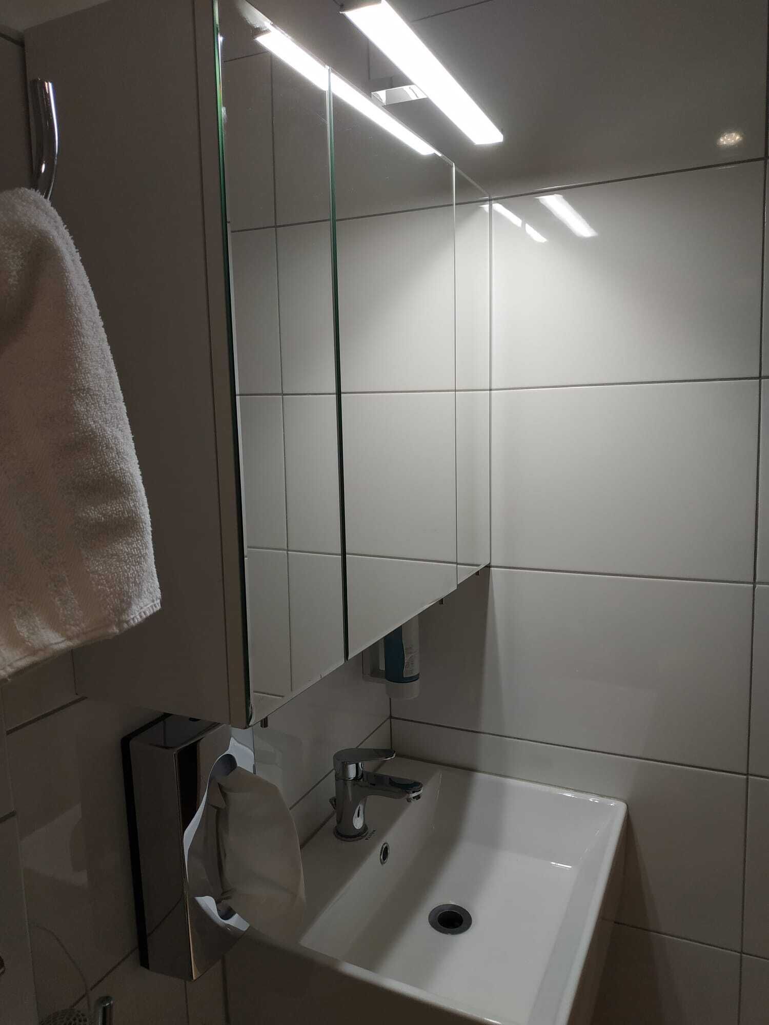 A bathroom with a white sink, a mirror, and a towel hanging on a rack.