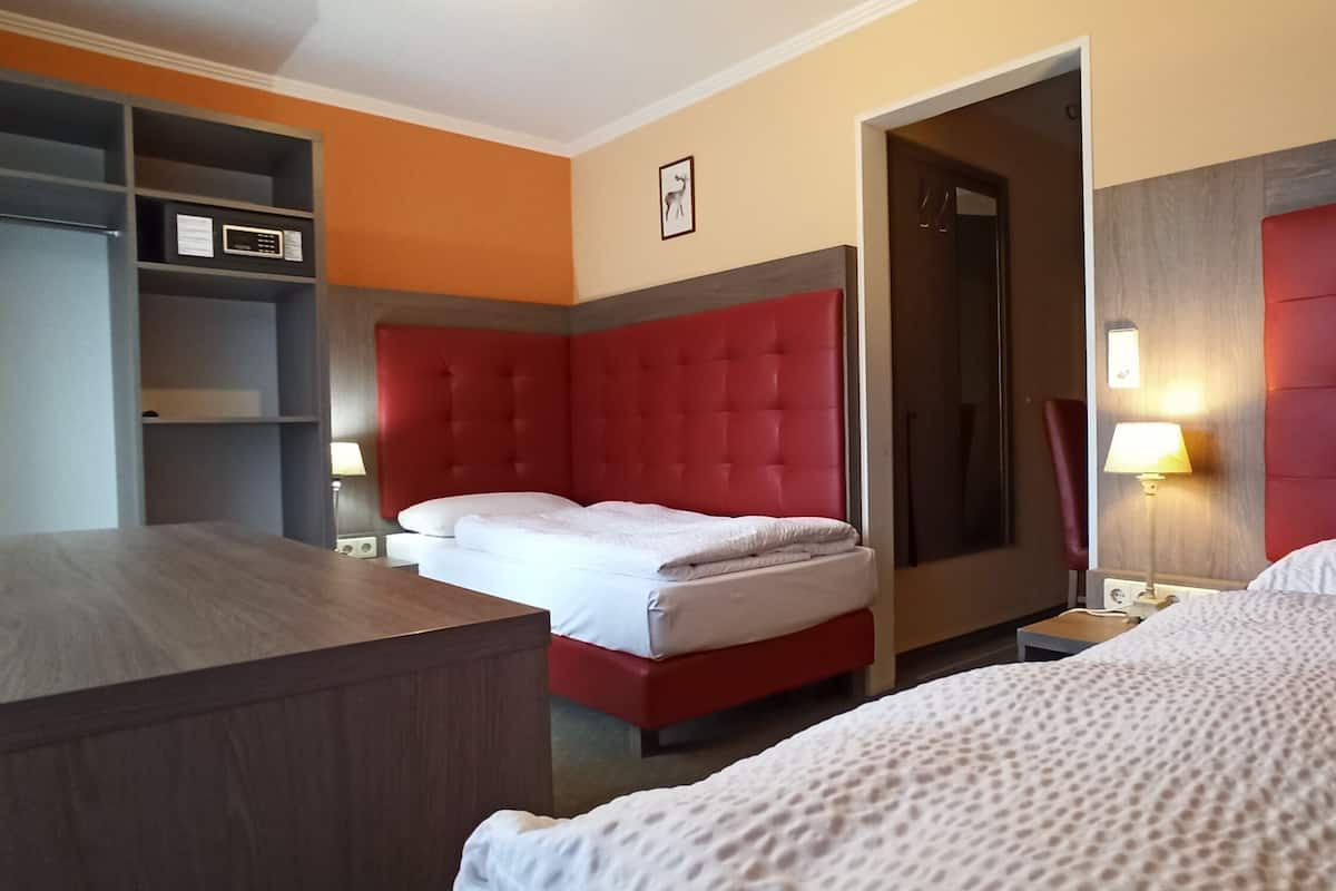 A hotel room with a red upholstered headboard, a wooden desk, a wardrobe, and a bed with white bedding.