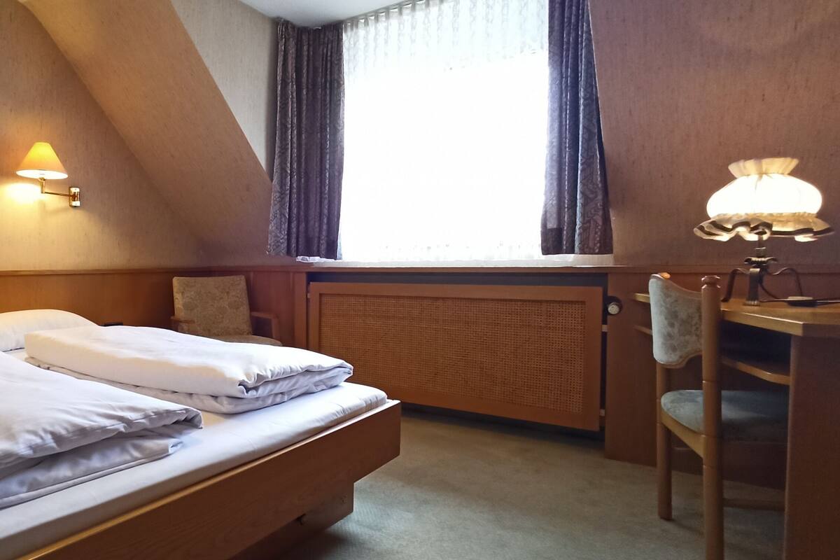 A hotel room with a bed, a desk, and two wall-mounted lamps.