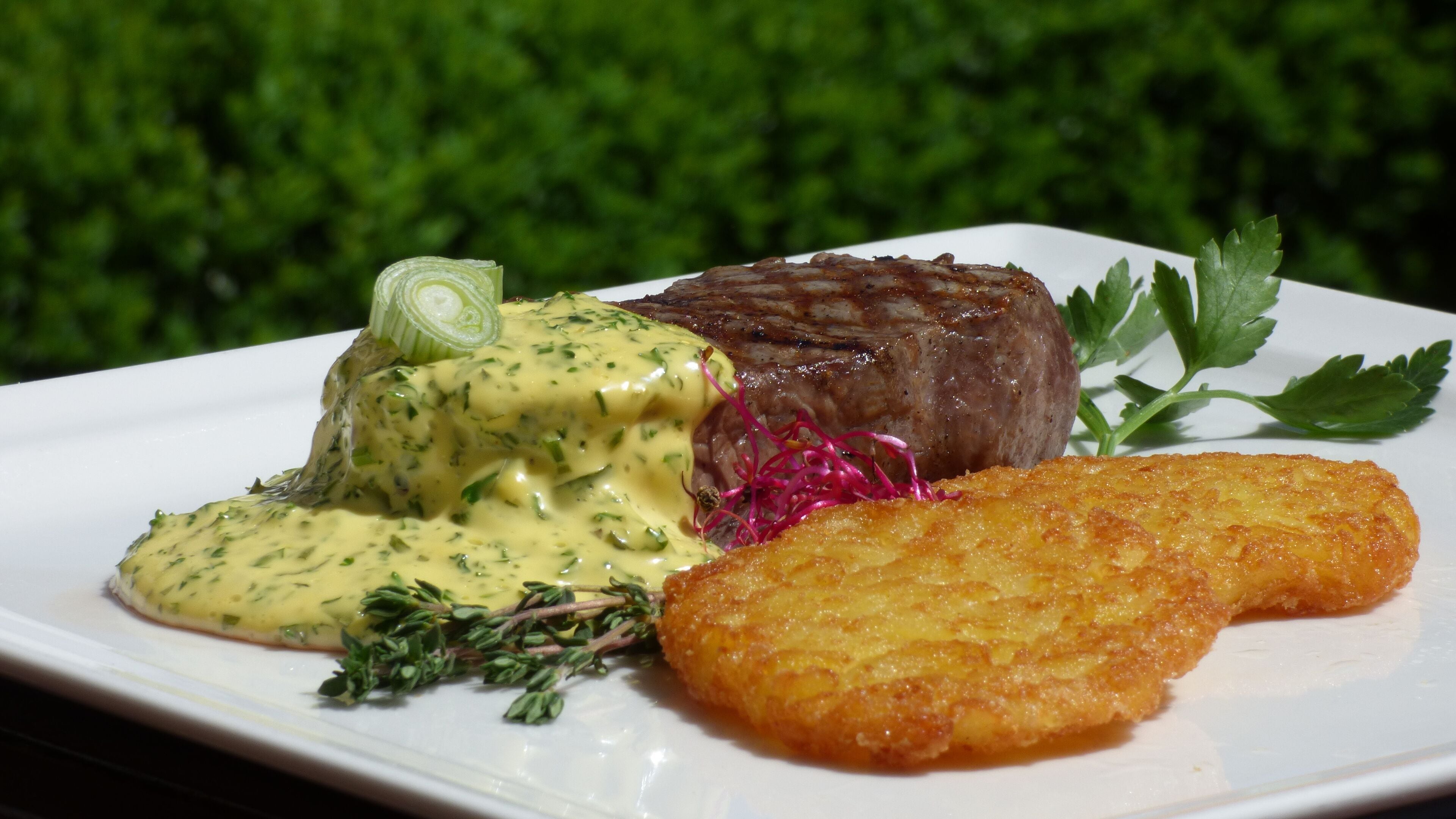 A plated meal with a steak, sauce, and a fried item, garnished with herbs and a green leafy vegetable.