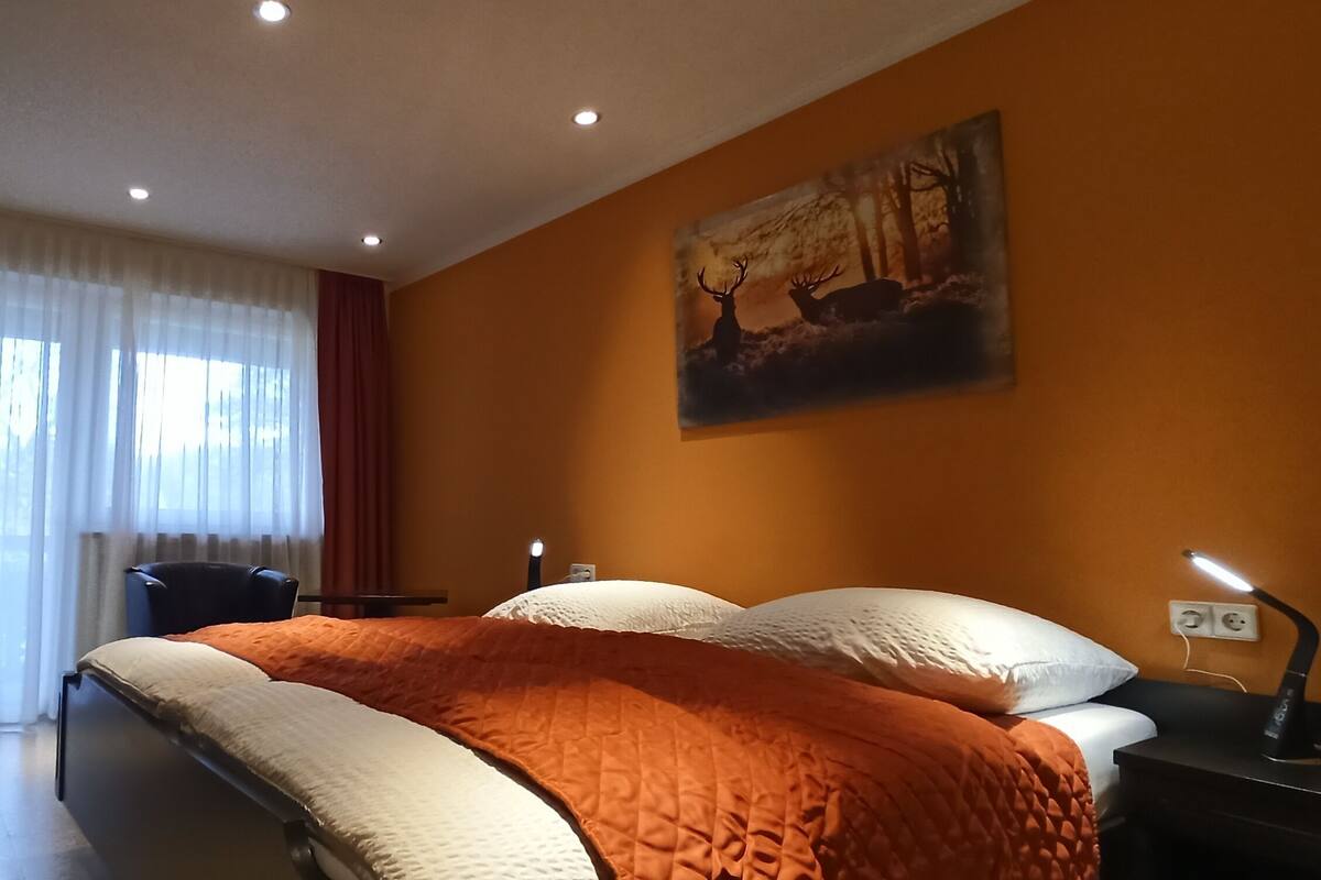 A hotel room with a bed, a desk, a chair, a TV, and a painting on the wall.