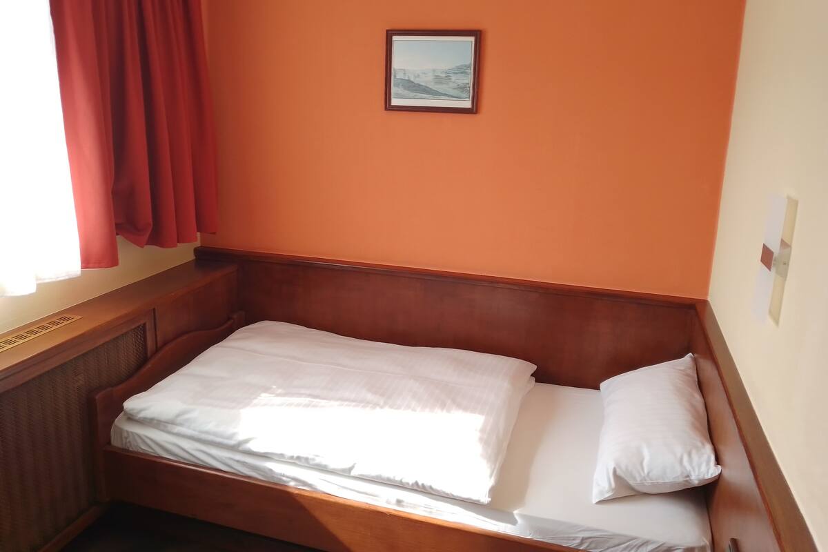 A single bed with white bedding in a room with orange walls and a wooden headboard.