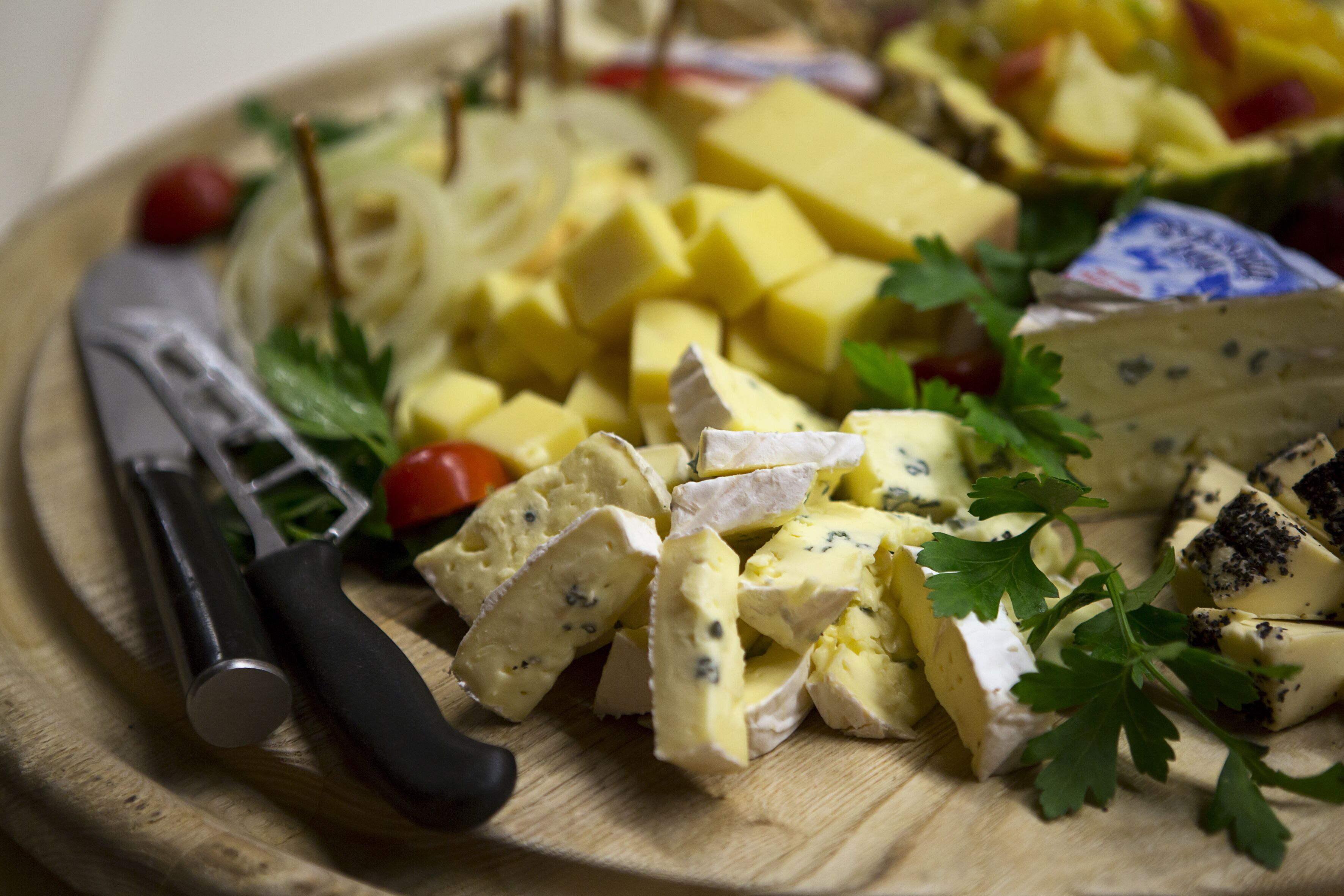 Une planche à découper en bois, sur laquelle on trouve différents fromages, un couteau et quelques herbes aromatiques.