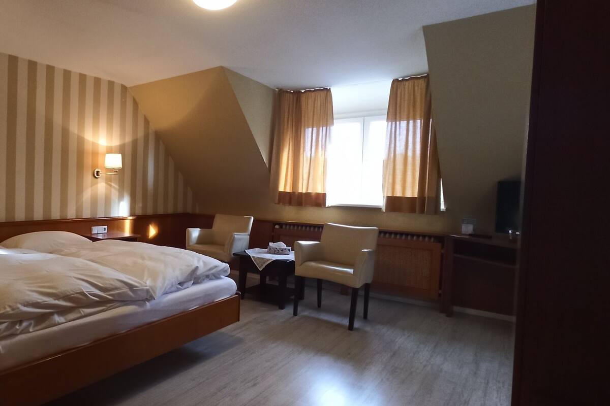 A hotel room with a large bed, a desk with a chair, a small table, and two wall-mounted lamps.