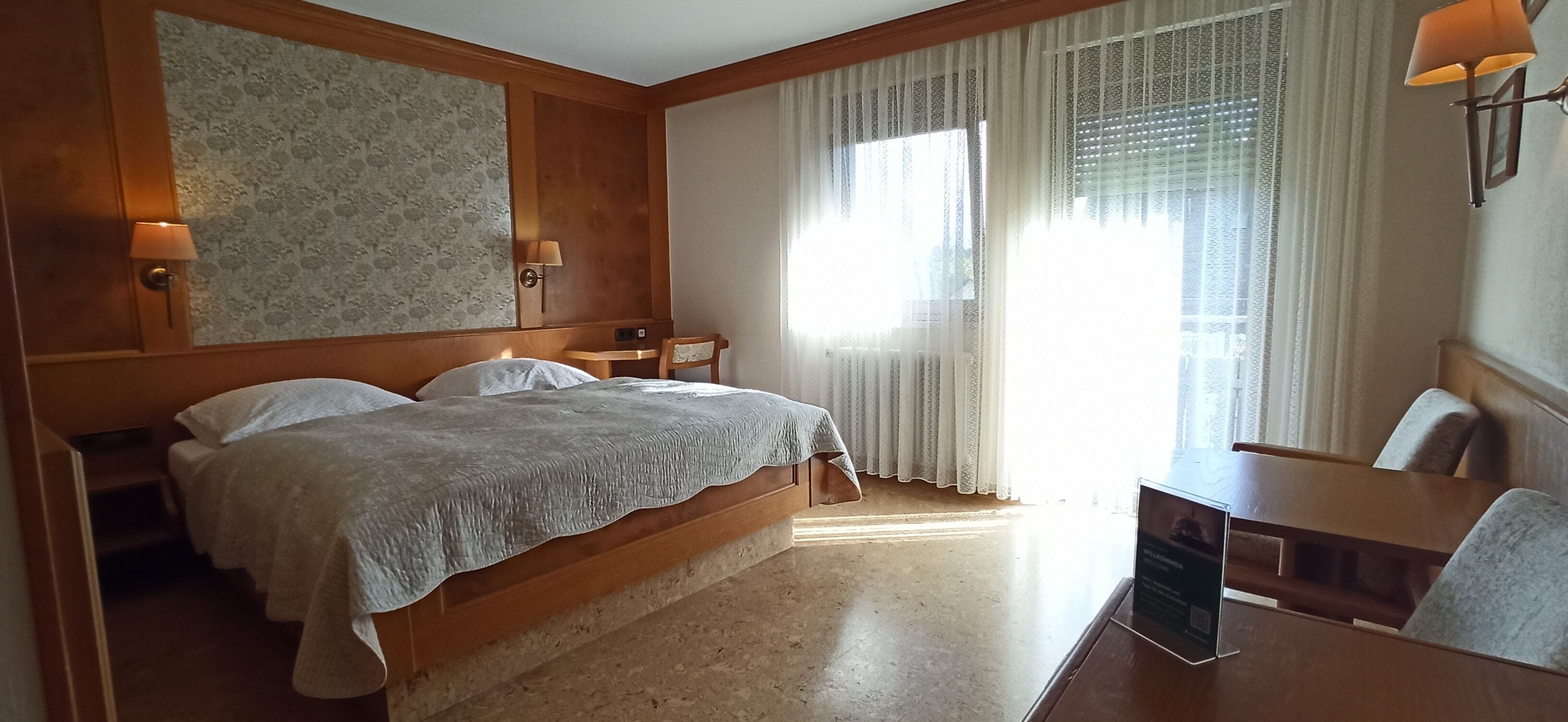 Ein Hotelzimmer mit einem großen Bett, zwei Nachttischen, einem Schreibtisch und einem Sessel.