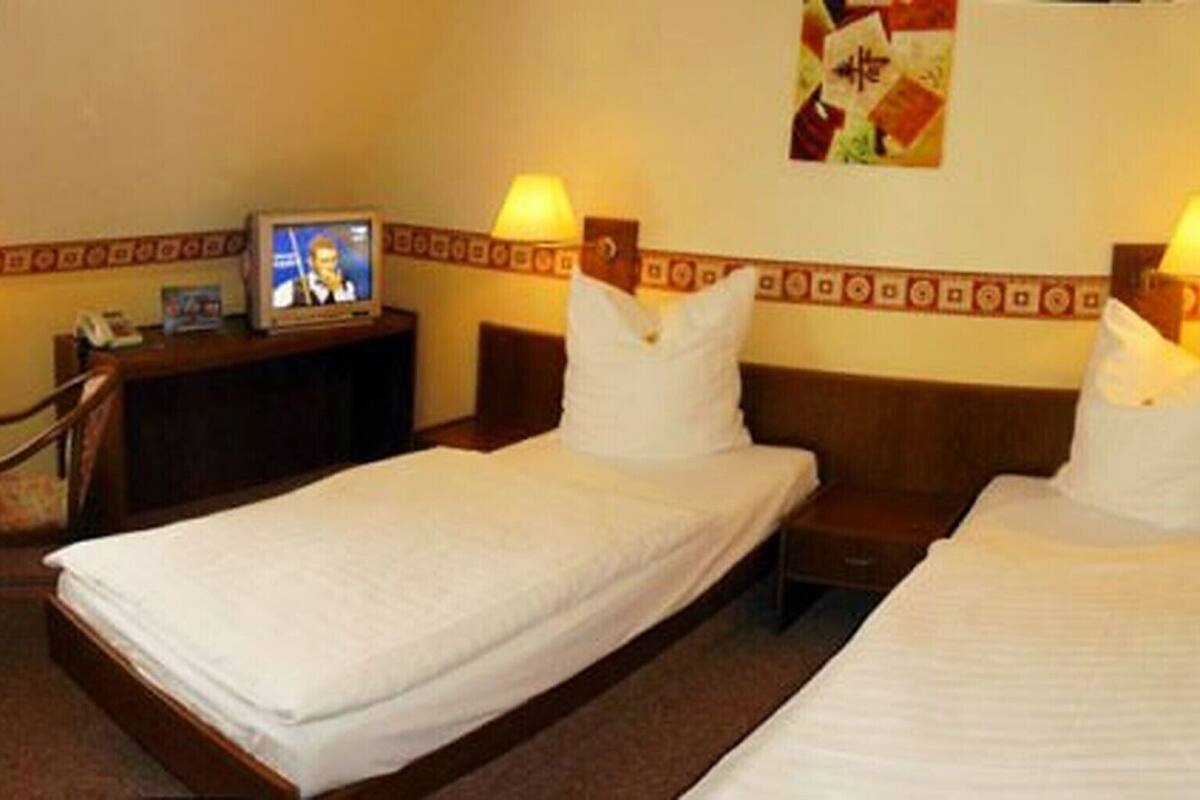A hotel room with two single beds, a small desk, a chair, and a television.