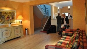 A hotel lobby with a wooden floor, a sofa with plaid cushions, a cabinet with decorative items, and a staircase leading to another area. - Hotel 4 Hufen (Schoenefeld)