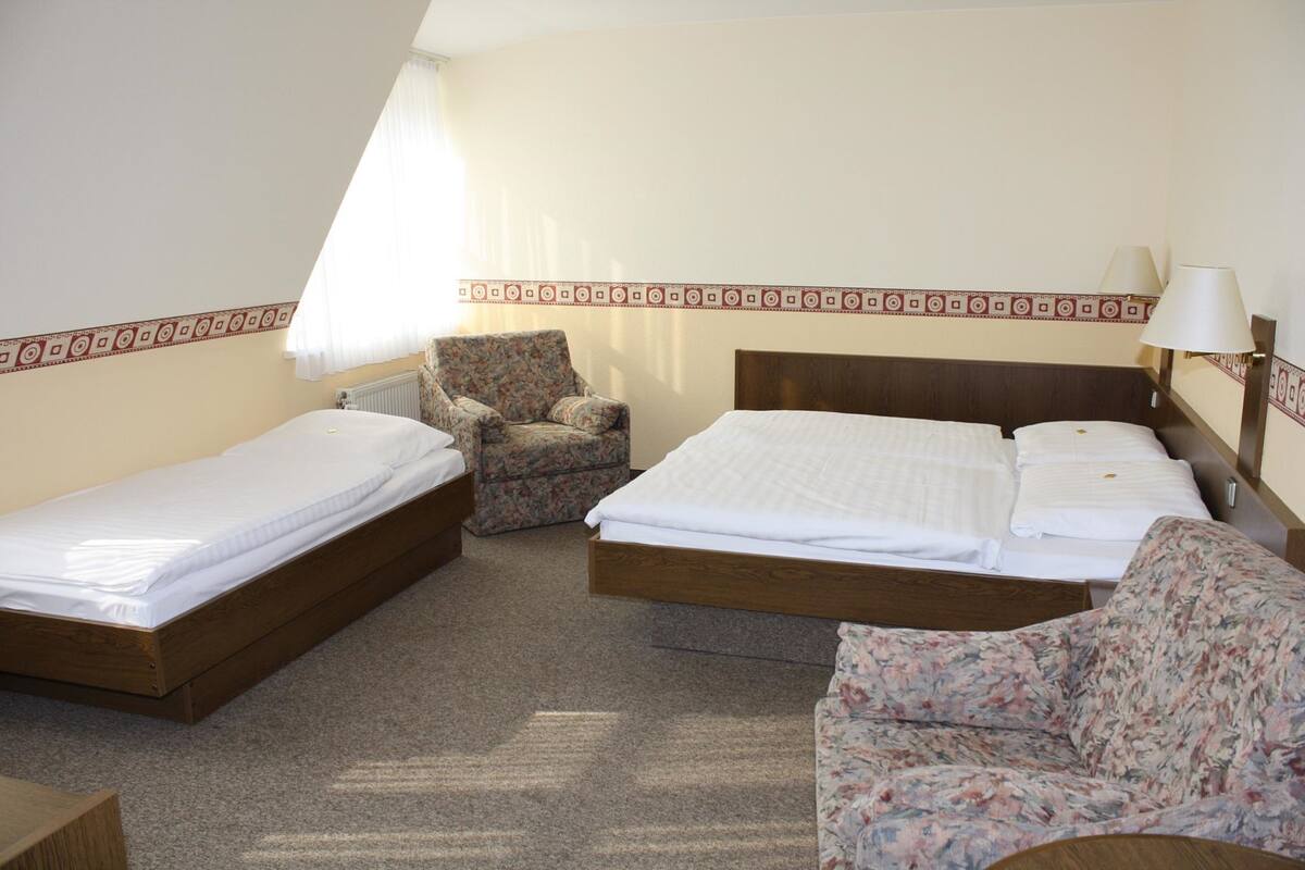 A room with two single beds, a floral armchair, and a wooden headboard.