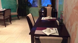 A dining area with a table set for two, chairs, a vase with flowers, and a window with a view of a car and trees. - Hotel-12-Apostel (Pforzheim)