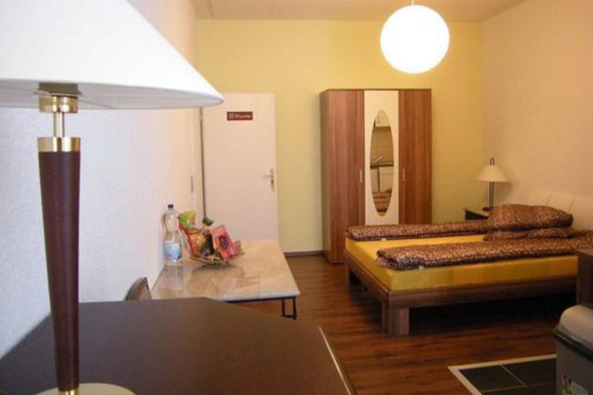 A compact hotel room with a single bed, a small table, a lamp, and a wardrobe.