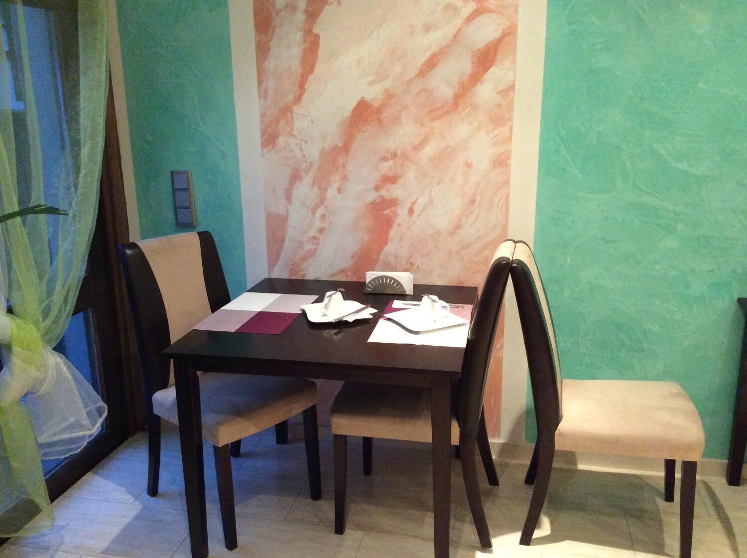 A dining area with a table set for four, chairs, a window with sheer curtains, and a wall with a marble-like pattern.