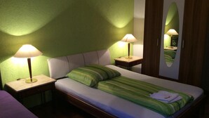 A neatly made bed with green striped bedding, two bedside lamps, a wooden nightstand, and a mirror on the wall. - Hotel-12-Apostel (Pforzheim)