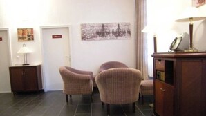 A hotel lobby with a check-in desk, two armchairs, a cabinet, and a wall-mounted artwork. - Hotel-12-Apostel (Pforzheim)