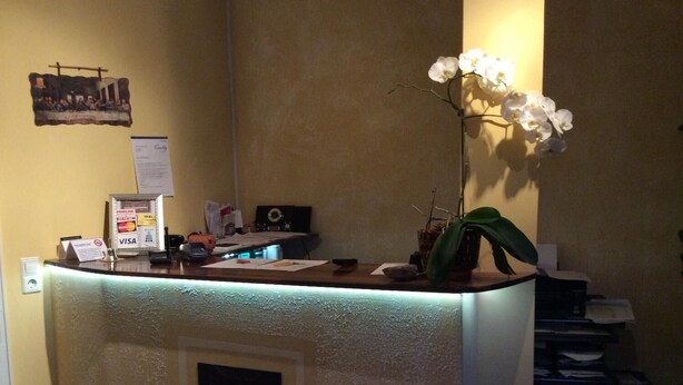 A reception desk with a lit-up counter, a framed picture on the wall, and a potted orchid on the desk. - Hotel-12-Apostel (Pforzheim)