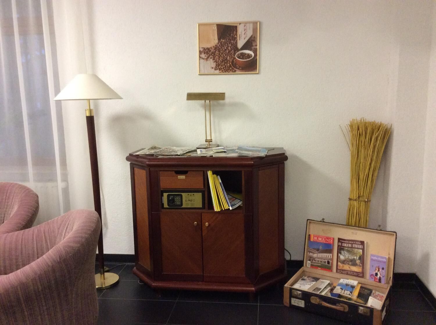 Ein Zimmer mit einem Holzschrank, einer Lampe, einem Bild von Kaffeebohnen, einem Besen und einer Bücherkiste.