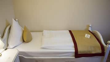 A single bed with a white mattress, a beige blanket, and a red trim. There is a small tag on the blanket.