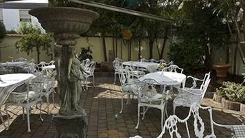 Un área de patio al aire libre con mobiliario de metal blanco, incluyendo mesas y sillas, y una maceta de piedra decorativa.